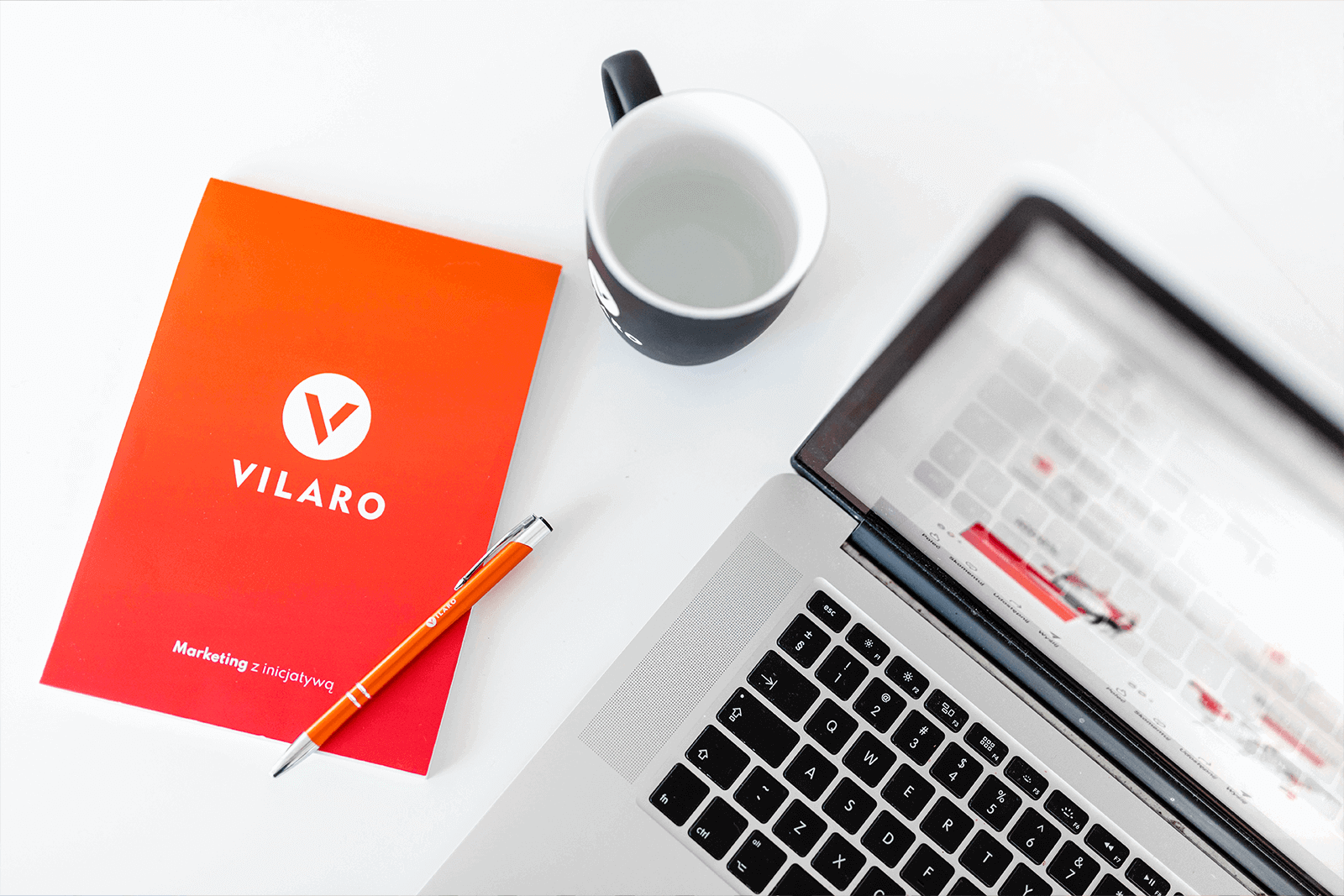 Laptop, kubek i notatnik z brandingiem firmy Vilaro - Marketing z inicjatywą.